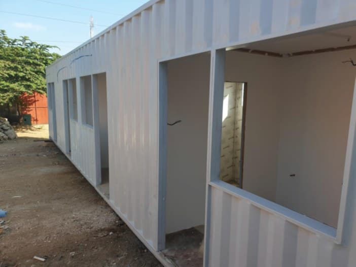 A long white container building with several window and door openings cut along its side, during fit-out.